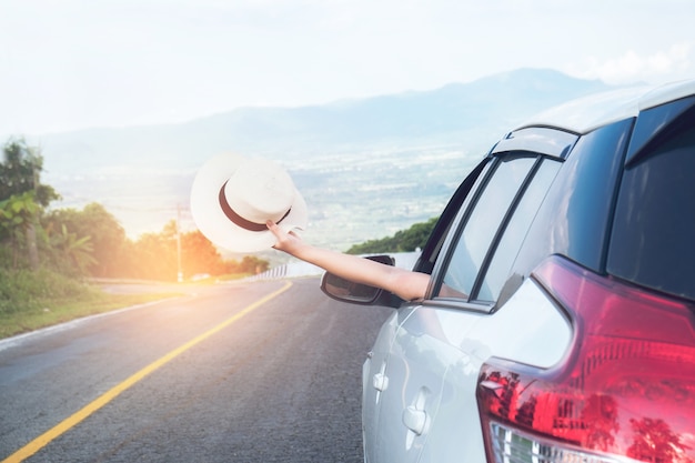 Joven hermosa chica asiática sosteniendo Hat tejido y llegar fuera del coche al atardecer