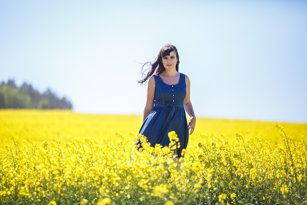 Joven hermosa chica feliz con un vestido azul en un floreciente campo de colza en verano