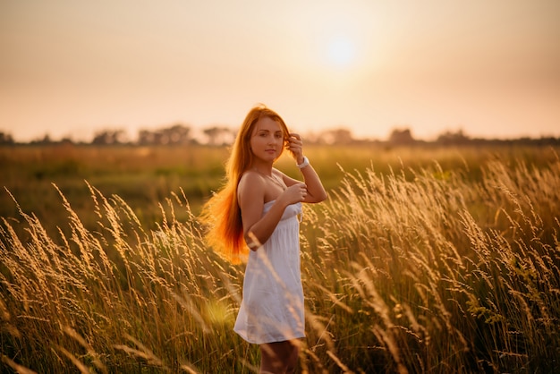 Joven hermosa chica pelirroja en un campo al atardecer