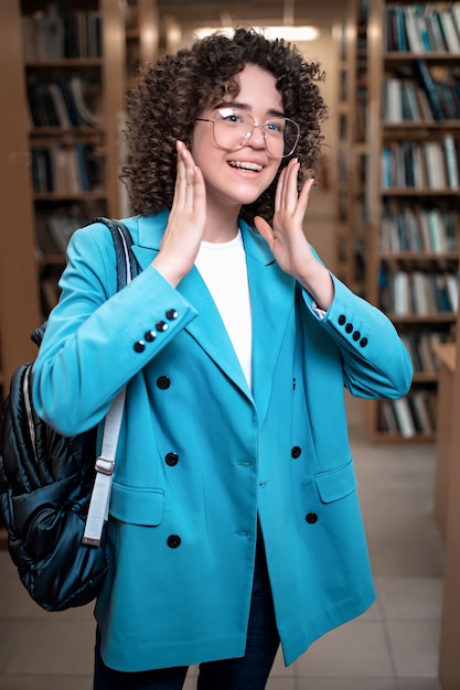 Joven hermosa chica rizada en vasos en una biblioteca