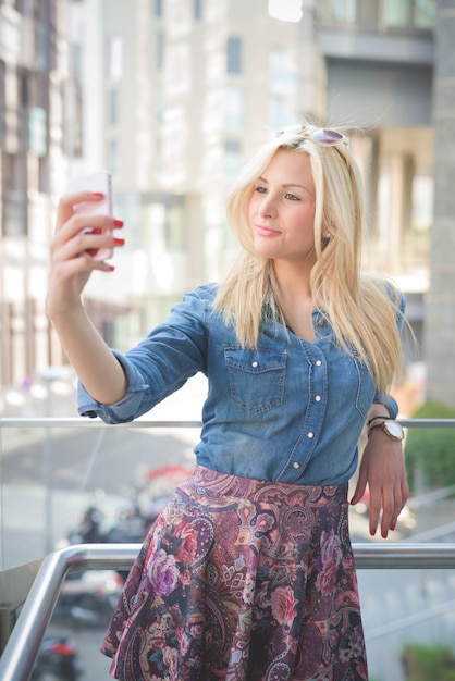 joven hermosa chica rubia caucásica usando un teléfono inteligente tomando un selfie
