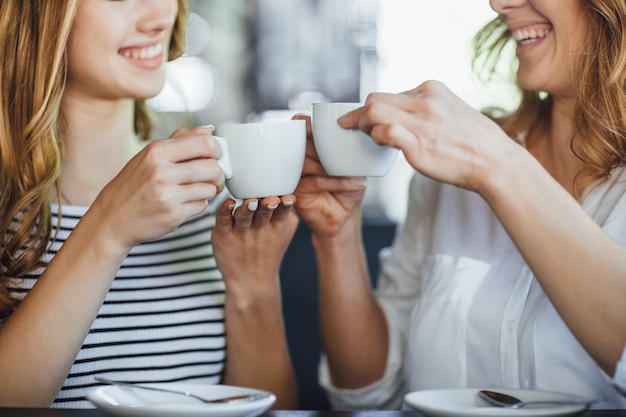 Joven hermosa chica rubia y su madre descansan en un café con terraza de verano, beben café y se comunican