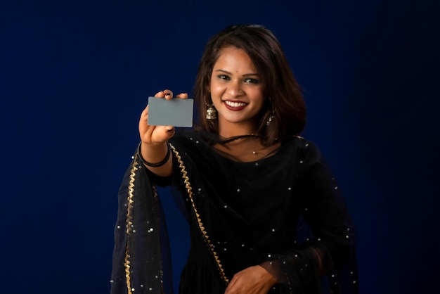 Joven hermosa chica sonriente posando con una tarjeta de crédito o débito sobre fondo azul.