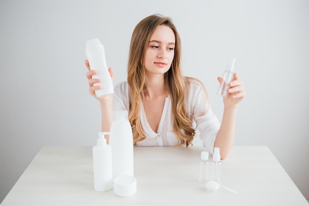 Una joven hermosa compara el tamaño de las botellas cosméticas para viajar para ahorrar espacio en la maleta. Viraje.