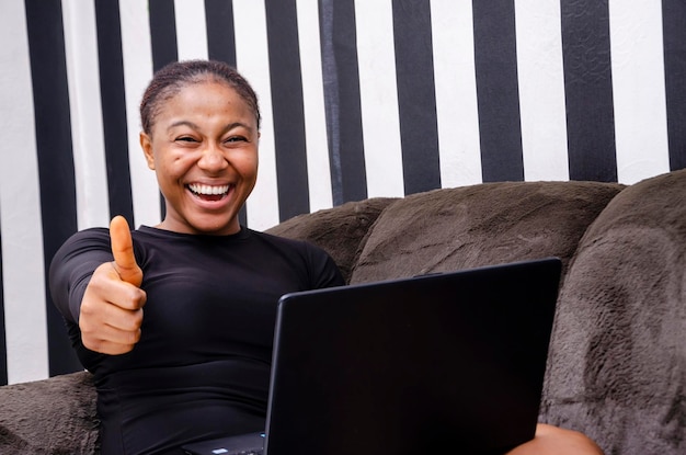 Joven hermosa dama africana que se siente abrumada por lo que vio en su computadora portátil e hizo el pulgar hacia arriba