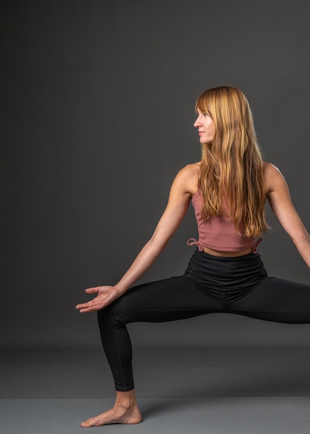 Una joven hermosa y delgada está haciendo yoga en un fondo gris