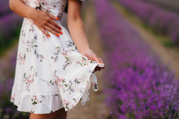 Una joven hermosa con un delicado vestido y un sombrero camina por un hermoso campo de lavanda y disfruta del aroma de las flores. Vacaciones y hermosa naturaleza.