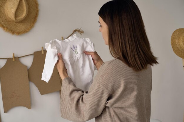 Una joven y hermosa diseñadora tiene ropa en sus manos y mira su calidad.