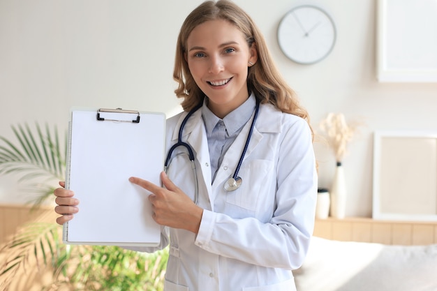 Joven hermosa doctora en bata blanca con fonendoscopio. El médico hace una videollamada, interactúa a través de Internet, habla con el paciente, brinda ayuda y ofrece asesoramiento en línea.