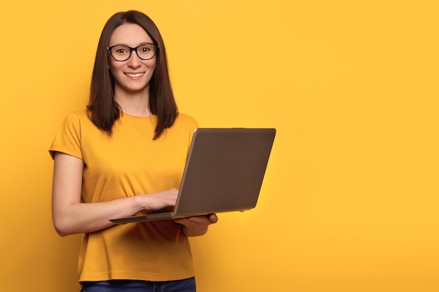 Una joven hermosa e inteligente que usa una computadora portátil aislada en un fondo amarillo