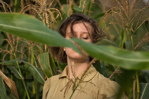 Foto joven hermosa y elegante con maquillaje dorado moderno en un campo de maíz verde sosteniendo los tallos con las manos