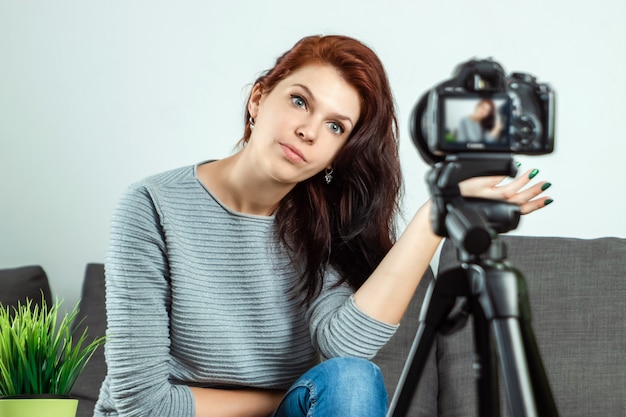 Una joven hermosa está sentada frente a una DSLR y graba un Vlog