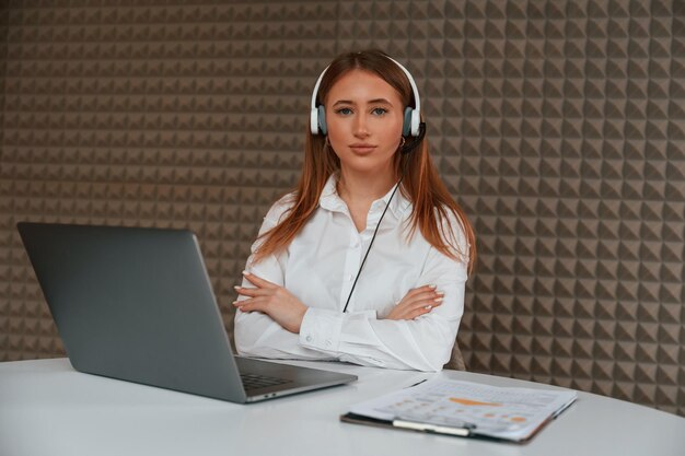 Una joven hermosa está sentada junto a una computadora portátil en la oficina.