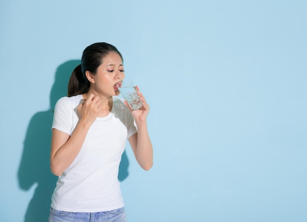 joven y hermosa estudiante que bebe agua helada y se preocupa por los problemas dentales sensibles que atacan de pie en el fondo de la pared azul.