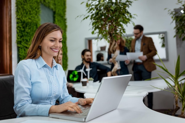 Joven hermosa y exitosa mujer de negocios sonriente analizando planes gráficos que muestran el éxito y trabajando en una laptop en la oficina.