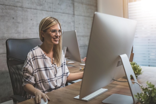 Joven hermosa y exitosa mujer de negocios sonriente trabajando en una computadora en la oficina.