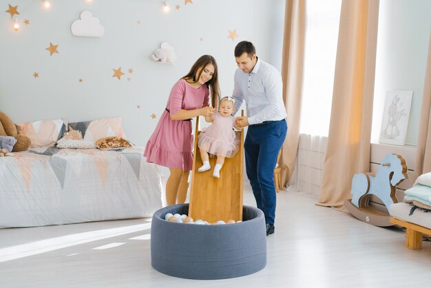 Joven hermosa familia caucásica jugando con su hija de un año en la habitación de los niños.