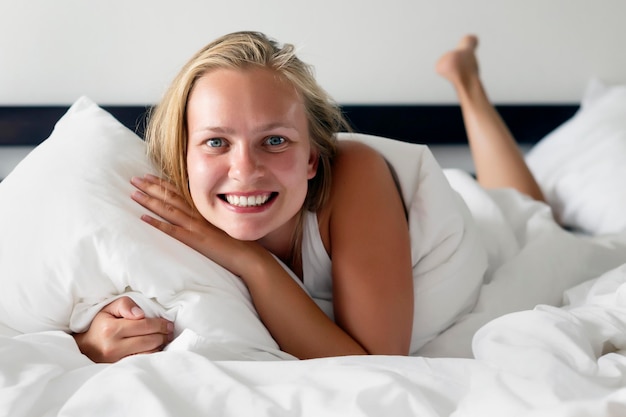 Una joven hermosa y feliz se acuesta en la cama y sonríe al espectador