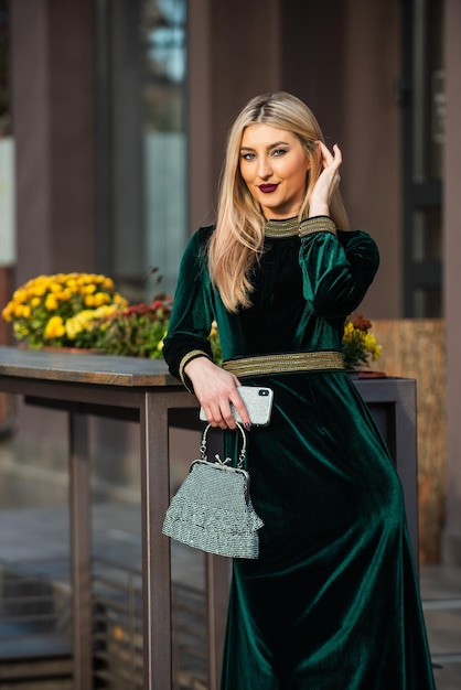 Joven y hermosa glamour terciopelo textil sexy mujer de negocios espera conocer la vida moderna al aire libre chica cuidado joya bolso de piedra o bolso glam embrague accesorio elegante mujer en vestido de terciopelo verde