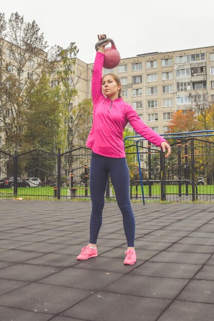 La joven hermosa haciendo ejercicios deportivos con pesas rusas fuera