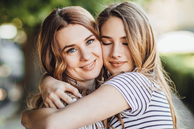 Una joven hermosa hija rubia abraza a su madre de mediana edad en las calles de la ciudad.