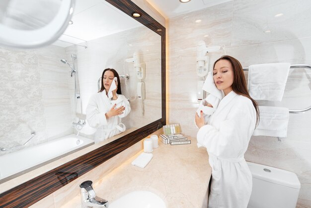 Una joven hermosa se lava la cara y sostiene una toalla en un hermoso baño blanco Buenos días frescos en el hotel Descanso y viajes Recreación y turismo del hotel