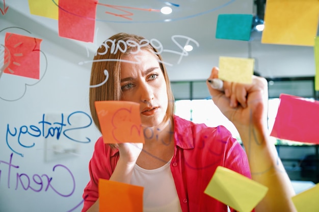 Joven y hermosa líder de negocios escribiendo una idea de marketing a bordo de la Inmaculada