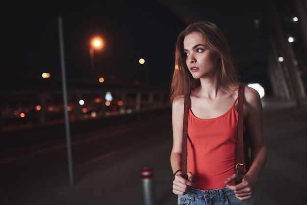 Una joven hermosa con una mochila detrás de sus hombros se encuentra en la calle cerca de un aeropuerto