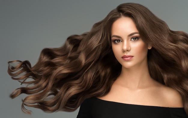 Joven hermosa modelo de cabello castaño con cabello largo y rizado bien cuidado y elegante maquillaje Excelentes ondas de cabello Arte de peluquería y cuidado del cabello