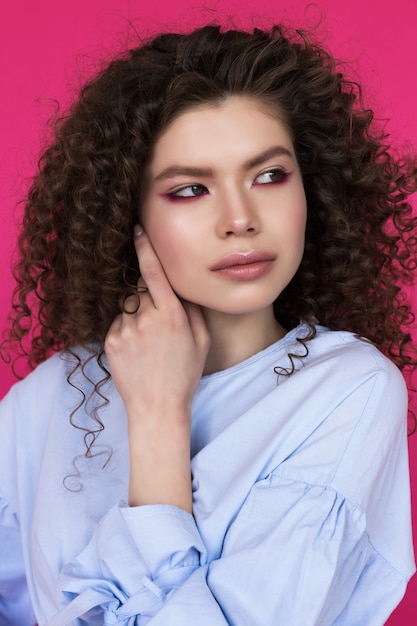 Joven hermosa modelo caucásico con peinado afro rizos vistiendo blusa azul sobre rosa