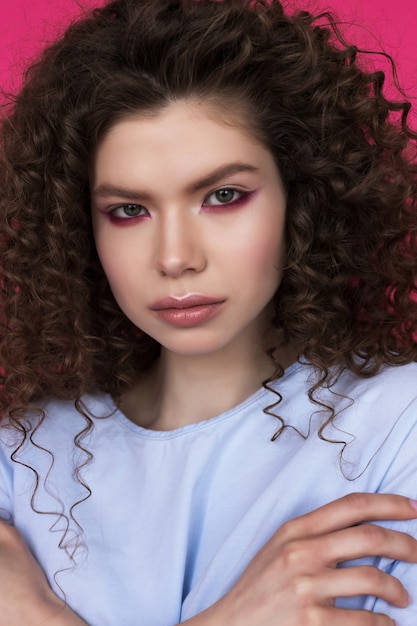 Joven hermosa modelo caucásico con peinado afro rizos vistiendo blusa azul sobre rosa