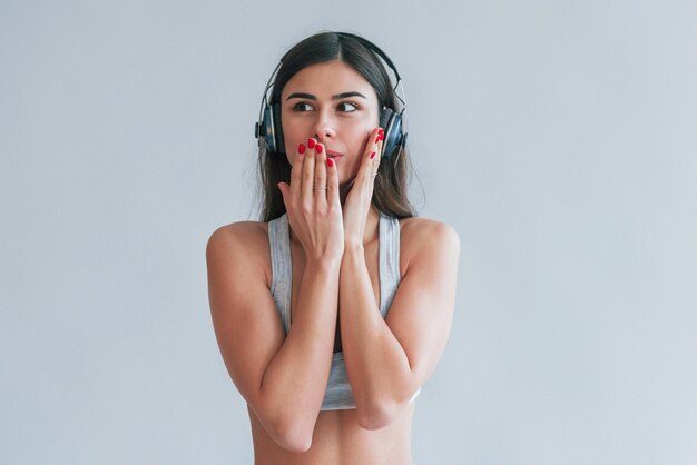 Joven hermosa morena en ropa interior y auriculares está en el interior del estudio con fondo blanco.