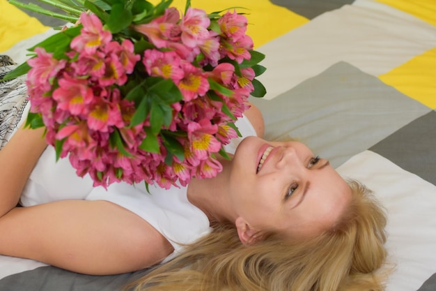 joven hermosa mujer se acuesta en la cama con un ramo de flores frescas