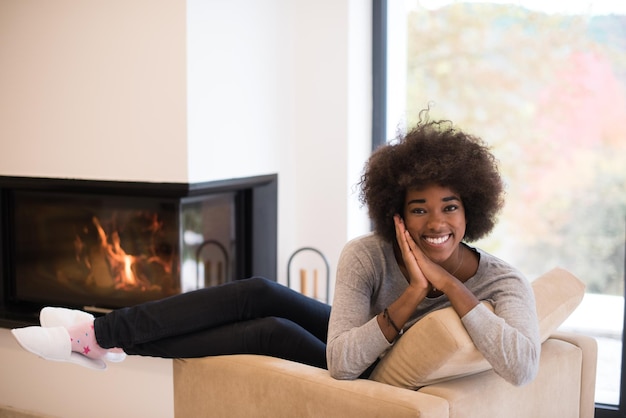 Joven hermosa mujer afroamericana relajándose en una silla frente a la chimenea en el día de otoño