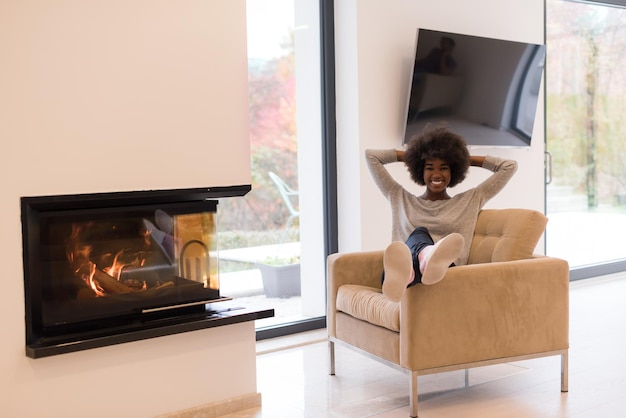 Joven hermosa mujer afroamericana relajándose en una silla frente a la chimenea en el día de otoño