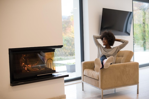 Joven hermosa mujer afroamericana relajándose en una silla frente a la chimenea en el día de otoño