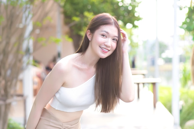 Joven hermosa mujer asiática con buena piel en camisa crema de pie sonriendo felizmente