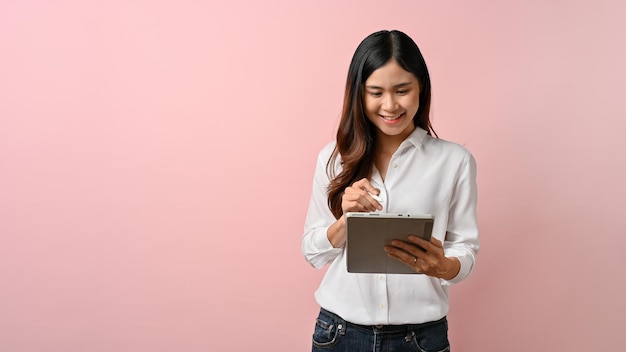 Joven hermosa mujer asiática escribiendo en tableta digital rosa fondo aislado