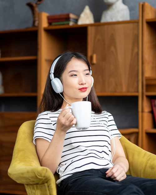 Joven hermosa mujer asiática escuchando música con auriculares, sentado en una silla