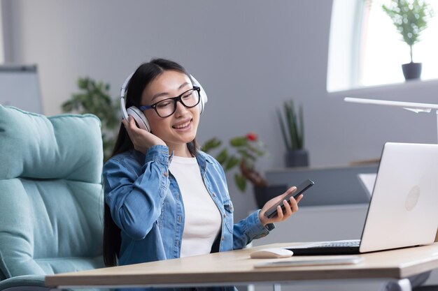 Joven hermosa mujer asiática escuchando música en la oficina usando el teléfono y la aplicación de música mujer de negocios