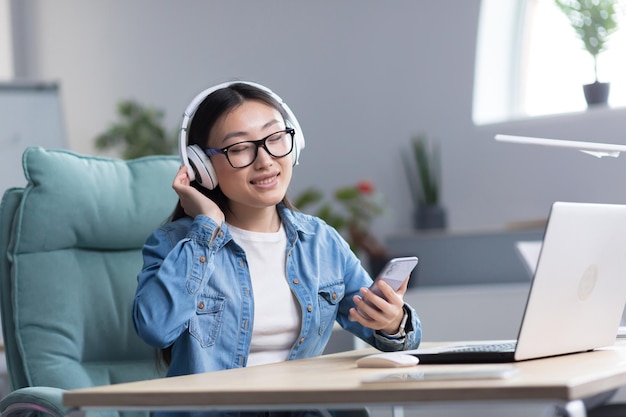 Joven hermosa mujer asiática escuchando música en la oficina usando el teléfono y la aplicación de música mujer de negocios