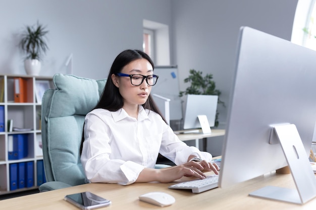 Una joven y hermosa mujer asiática está trabajando en una computadora en el director de la empresaria de la oficina