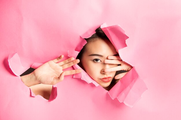 Foto joven hermosa mujer asiática expresión a través de un agujero de papel rasgado