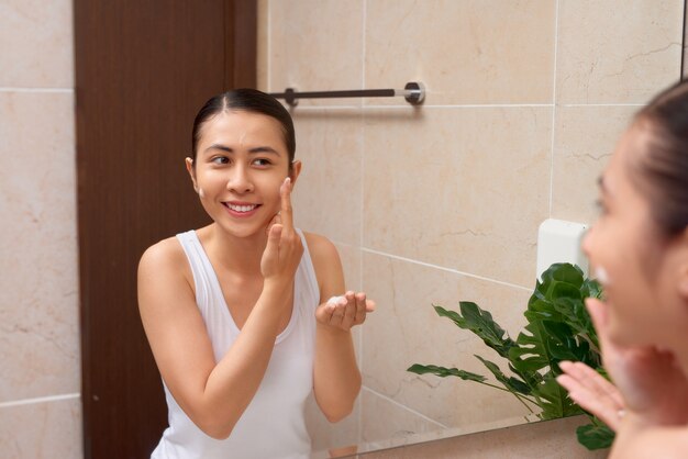 Joven hermosa mujer asiática lavándose la cara con las manos con jabón
