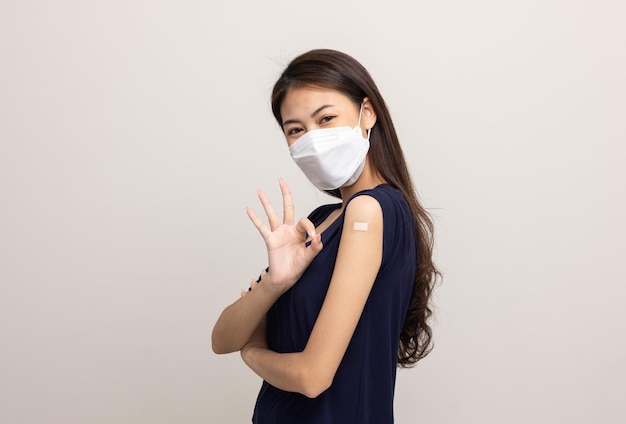 Joven hermosa mujer asiática con máscara y recibiendo una protección de vacuna contra el coronavirus Mujer feliz mostrando el brazo con vendaje después de recibir la vacunación sobre fondo blanco aislado