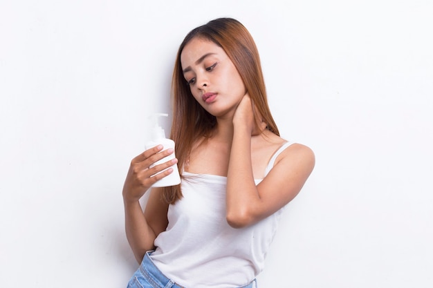 Joven hermosa mujer asiática poniendo productos para el cuidado de la piel en la cara aislado sobre fondo blanco.