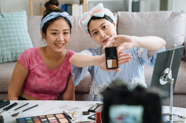 Joven hermosa mujer asiática profesional vloguera de belleza con amiga bloguera grabando un video tutorial de maquillaje para compartir en las redes sociales. señora con productos cosméticos que muestran a la cámara profesional.