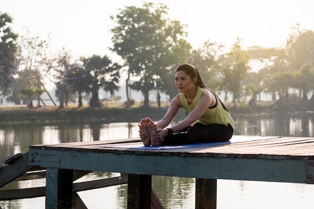 Foto joven hermosa mujer asiática en ropa deportiva haciendo yoga al aire libre en el parque por la mañana con luz solar cálida para un estilo de vida saludable. mujer joven, yogui, hacer, yoga, en, mañana, parque