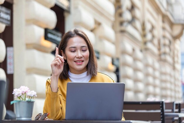 Joven hermosa mujer asiática sentada en una cafetería en una mesa de madera tomando café y usando una laptop