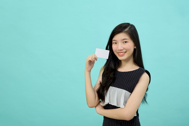 Joven hermosa mujer asiática sonriendo, mostrando, presentando tarjeta de crédito para realizar pagos o pagar negocios en línea sobre fondo azul.